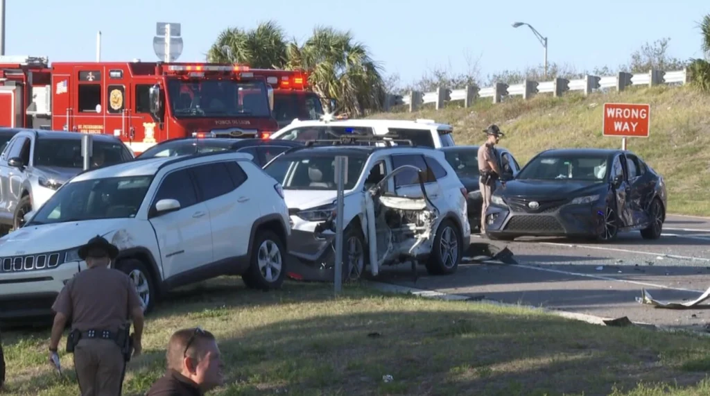 Scene of a multi-car accident on I-275 in St. Petersburg with damaged vehicles, emergency responders, and a "Wrong Way" sign in the background.